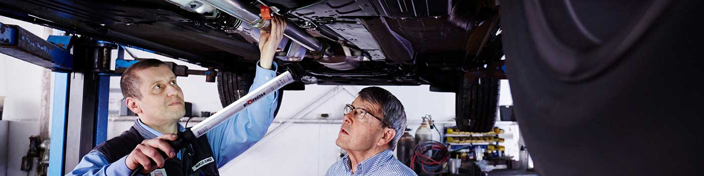 Zwei Mitarbeiter gucken unter ein Auto, welches auf einer Hebebühne steht