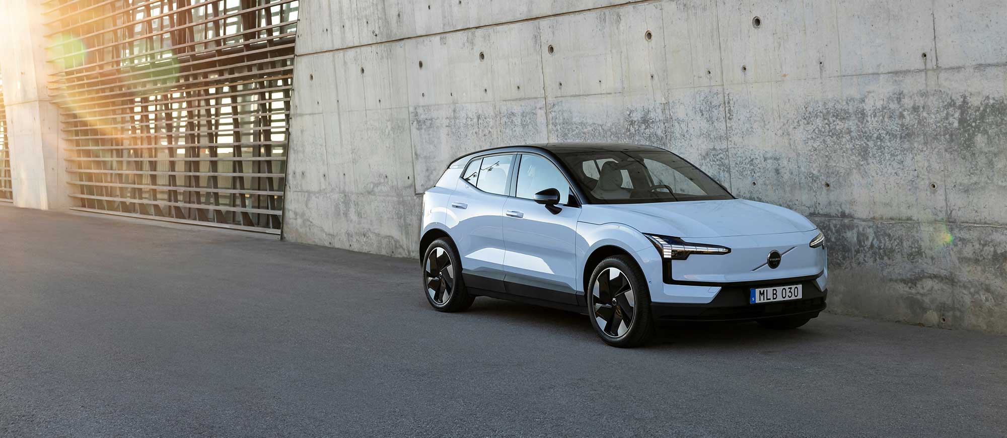 Volvo Ex30 steht vor einer Wand, im Hintergrund scheint die Sonne